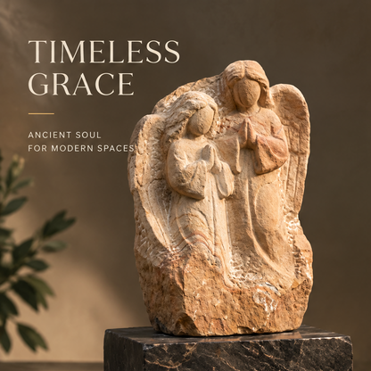 VITALUXO Raw Stone Angel Relief Sculpture front view on dark marble base with olive plant in warm interior light — Timeless Grace, Ancient Soul for Modern Spaces